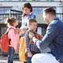 Young parents saying goodbye to their little children near school