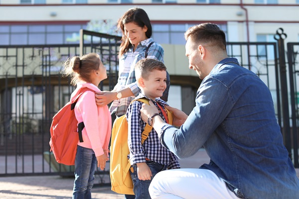 Young parents saying goodbye to their little children near school